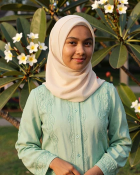 Young Bruneian woman in elegant modest fashion smiling in tropical garden setting