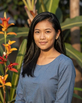 Burmese woman in casual blue blouse smiling warmly in a Yangon garden